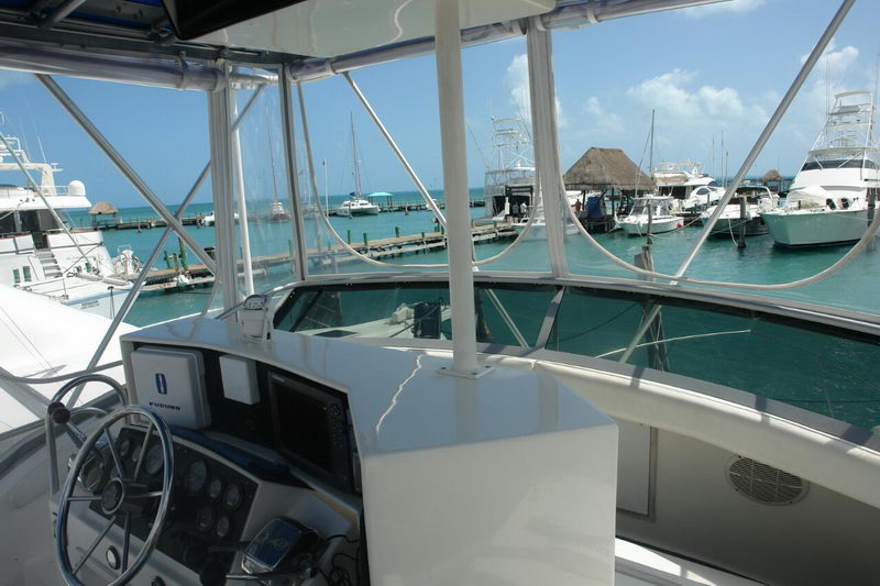 Vista desde el puesto de mando del flybridge del Bertram 34 con volante, electrónica y manómetros sobre la marina de Isla Mujeres y agua turquesa