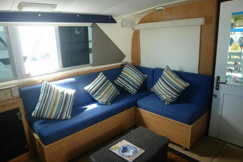 Salón interior con aire acondicionado del Bertram 34 con sofá en L azul, cojines a rayas y acabados de madera para descansar entre capturas