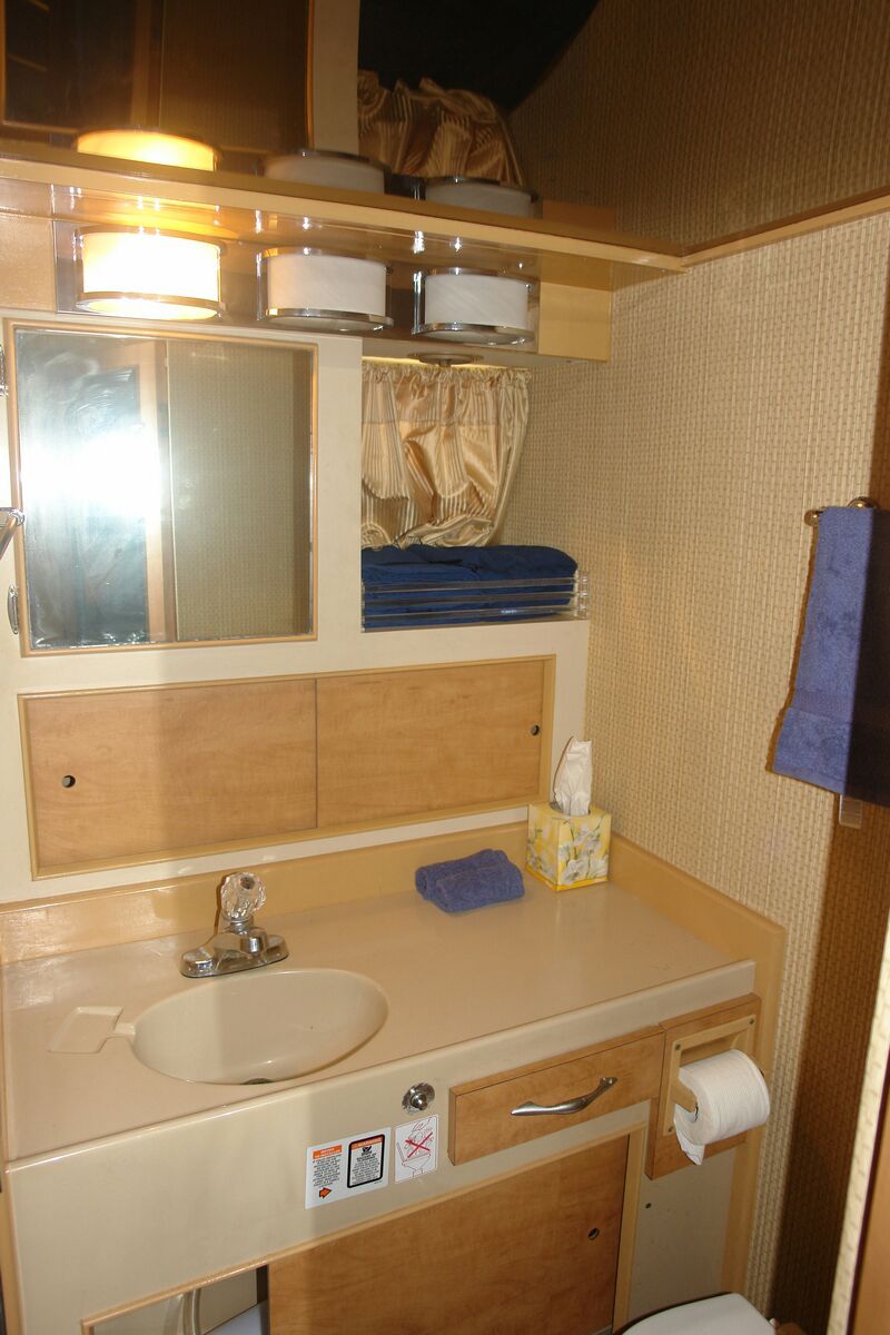 Baño privado y tocador a bordo del Bertram 34 con lavabo, espejo, toallas dobladas y carpintería de madera, charter de pesca en Cancún
