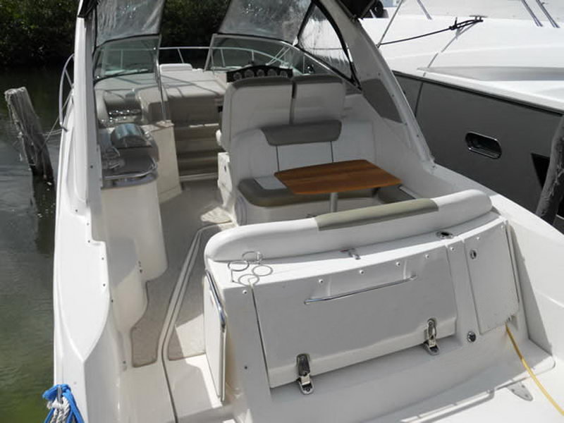 Cockpit of a Sea Ray cruiser looking aft, with grey and tan vinyl seating, a teak cockpit table, a wet bar and a transom sun lounge, shaded by the camper canvas.