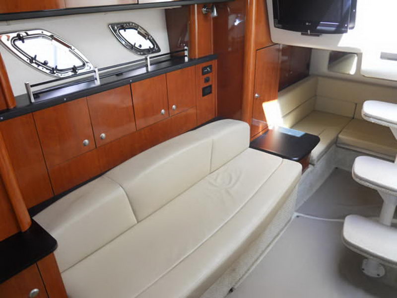 Interior salon of a Sea Ray cruiser with a cream leather sofa, glossy cherry wood cabinets, opening portholes, a wall-mounted flat TV and carpeted steps leading up.