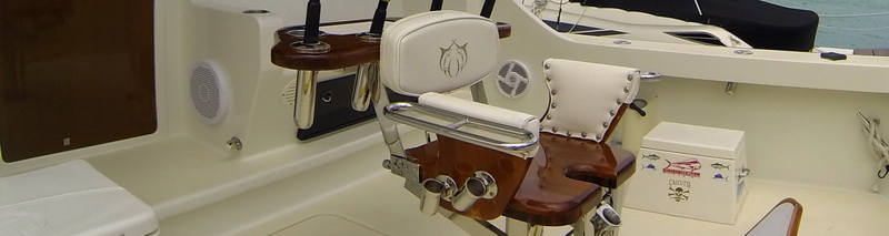 Tight crop of a sportfishing boat's cockpit showing a white fighting chair with a fish-logo headrest, rod holders, a wood and stainless mount, and a cooler. Cream fiberglass deck; partial view only.