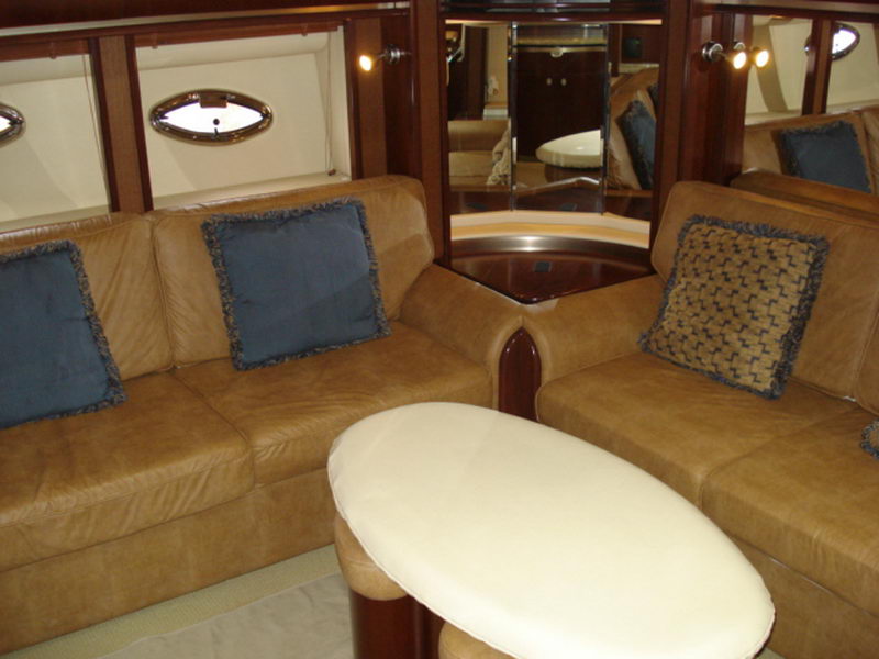 Interior salon of a Sea Ray with tan leather sofas, blue and patterned throw pillows, a cream oval table, mirrored bulkhead with oval portlights and glossy cherry trim. Warm, plush cabin.