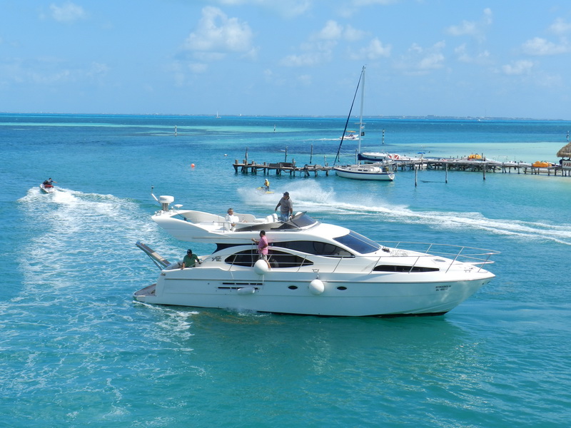 50 ft Azimut flybridge yacht cruising the turquoise Caribbean near Isla Mujeres pier with sailboats behind, Cancun luxury charter