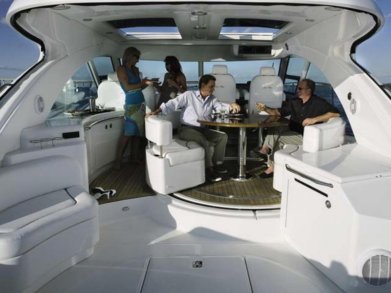 Invitados disfrutando cócteles en el salón abierto del yate Sea Ray 55 pies bajo su techo panorámico, renta de yates de lujo en Cancún