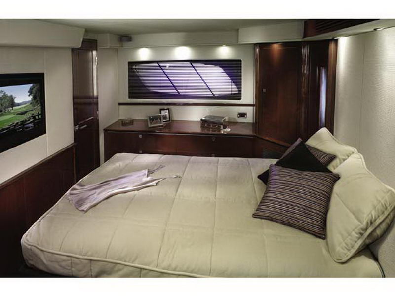 Guest cabin aboard Sea Ray 55 ft Laima yacht rental with queen bed, flat-screen TV and elegant dark wood finish