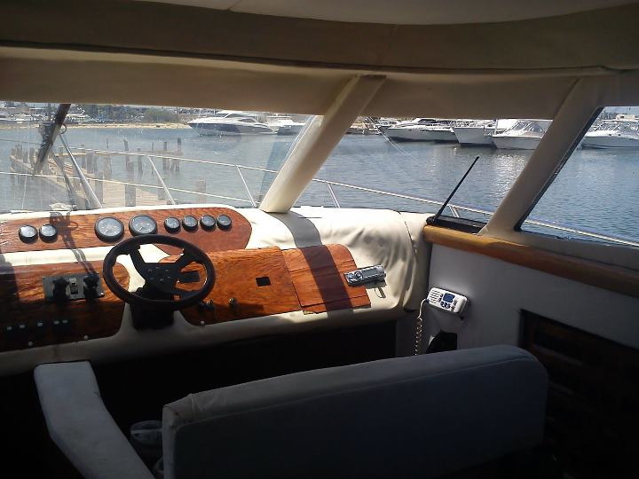 Helm station of Sealine 55 ft yacht rental showing teak wood dashboard, steering wheel and marina view from cockpit