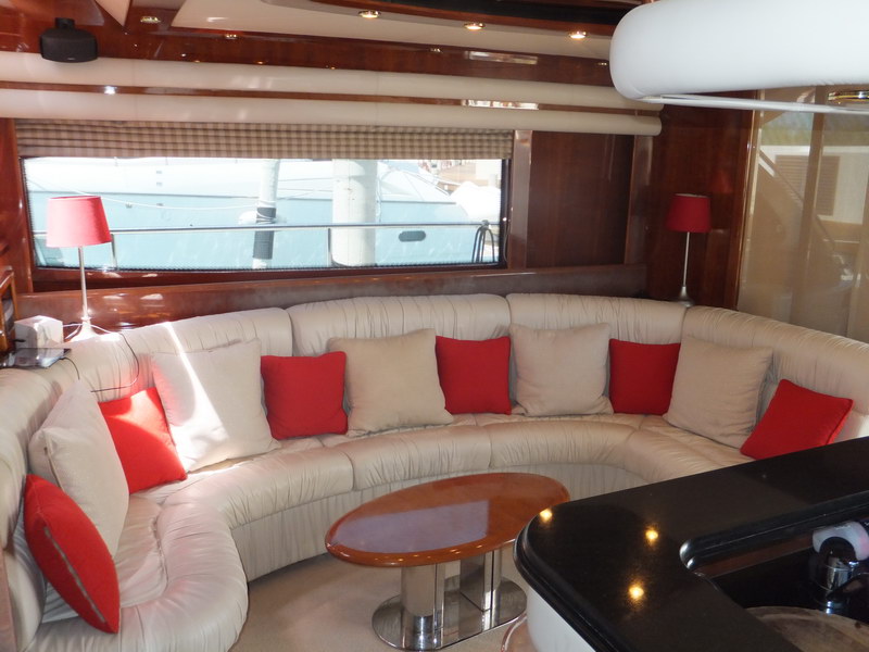 Curved cream sofa lounge of Nuvaris 63 ft luxury yacht with red accent cushions, teak coffee table and red lamps