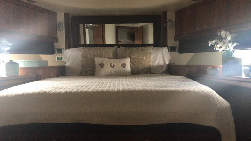 Master stateroom of Sunseeker 64 ft yacht with king bed, shell pattern cushion, mirror headboard and dark wood cabinets