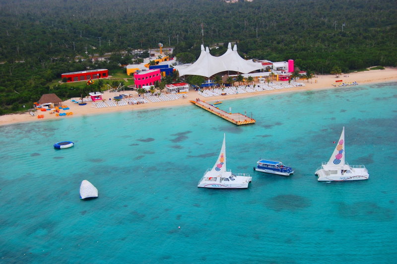 Vista aérea del club de playa Playa Mia en Cozumel con carpa blanca, playa de arena y catamaranes Aqua Dream sobre agua turquesa