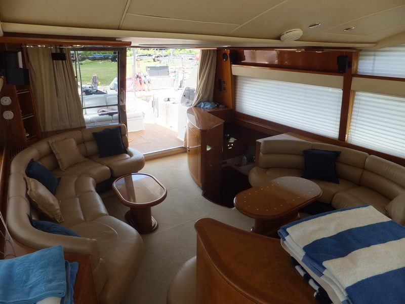 Lower salon of Azimut 60 ft yacht rental with tan leather sofas, oval wood coffee tables and rolled beach towels for guests