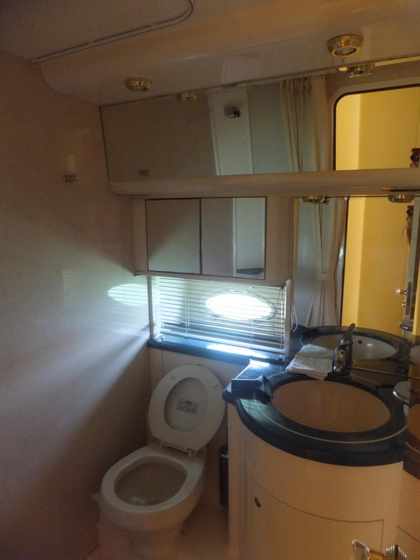 Bathroom aboard Azimut 60 ft charter yacht with toilet, circular vanity unit, round porthole and mirrored medicine cabinet
