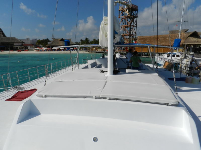 Proa del Catamarán Samba 3 con zona de asoleamiento acolchada, beach club de Isla Mujeres al fondo, charter de vela Cancún tours en grupo