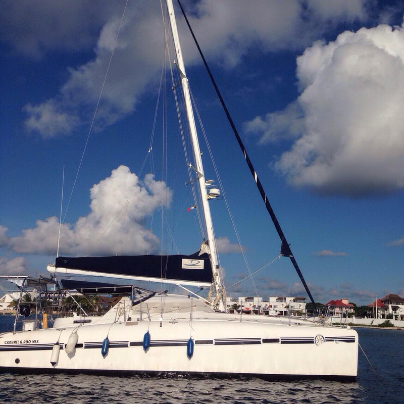 Perfil lateral del catamarán Lavezzi 42 en Cozumel mostrando el alto mástil y los cascos gemelos bajo nubes brillantes