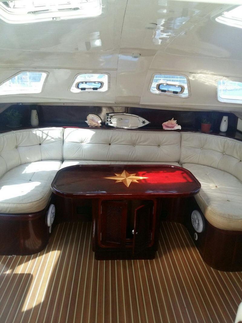 Salón interior del catamarán Lavezzi 42 con asientos de piel blanca y mesa de madera barnizada con incrustación de rosa de los vientos