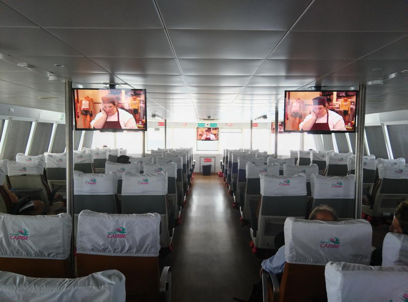 Amplia cabina cerrada del ferry a Cozumel con filas de asientos acojinados y pantallas de TV para el cruce de 45 minutos