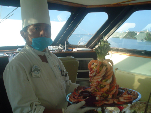 Chef presentando una torre de camarones armada alrededor de una piña en el puente del Discovery con vistas al mar de día