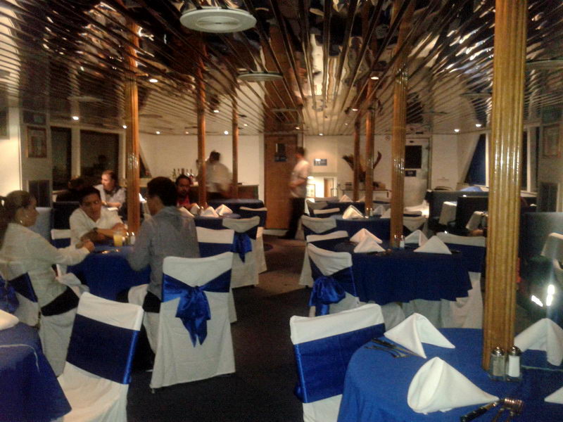 Salón comedor del barco Discovery con sillas vestidas de azul y blanco y mesas montadas para una cena de grupo nocturna