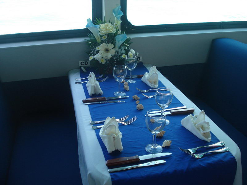 Three-tier pale-blue fondant wedding cake decorated with white sugar starfish and seashells, set on a foil board on a royal-blue and white draped table.