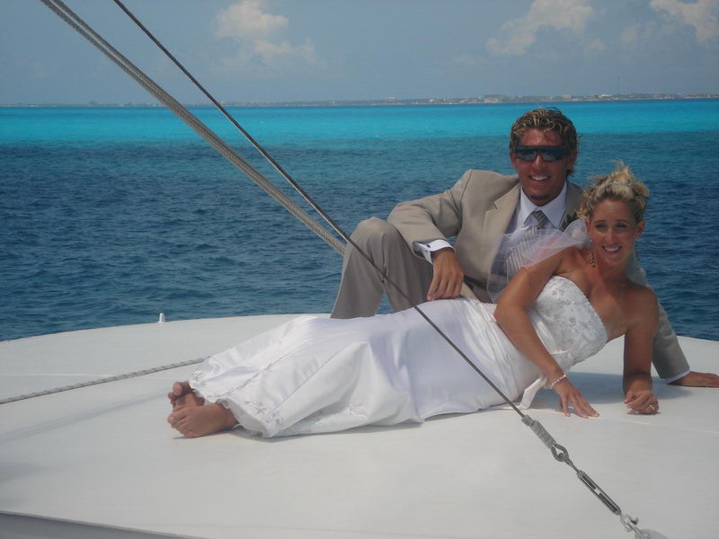 Bride and groom standing together posing on the white bow of the boat, bride in white gown and groom in tan suit, turquoise open sea and blue sky behind. Similar to wedding-20.
