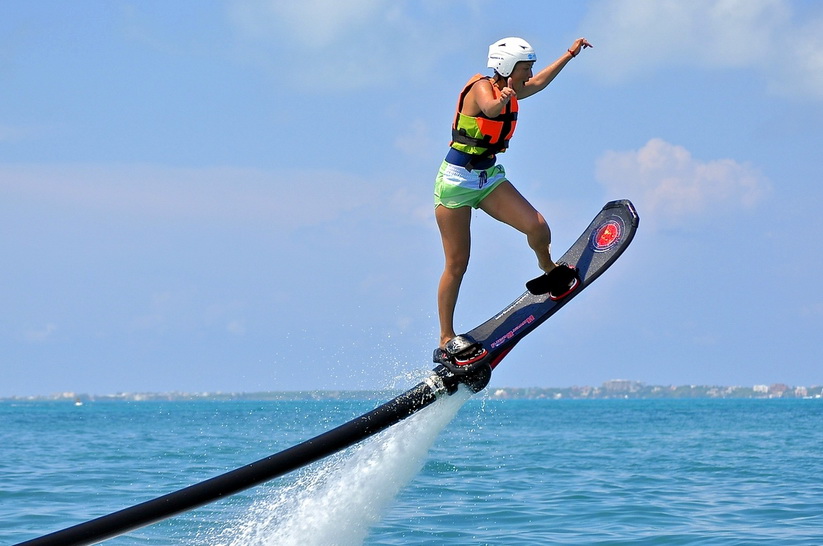 Rider carving on a water-powered hoverboard above the bright turquoise Caribbean off Cancun wearing a helmet and life vest