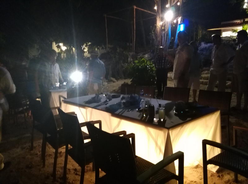 Private evening event at Sunset Grill Isla Mujeres, a long candlelit table set on the sand under string lights as guests gather
