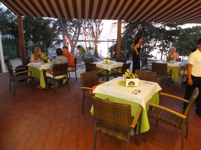 Covered wooden terrace at Sunset Grill Isla Mujeres with green-and-white set tables, diners and a sunset view over the Caribbean lagoon