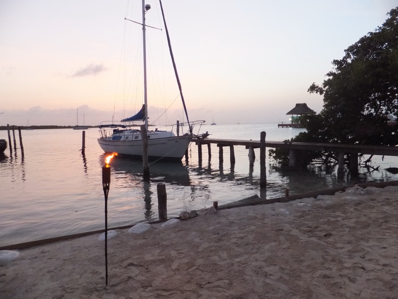 Sunset over a sailboat docked at the wooden pier with a tiki torch on the sandy shore near Sunset Grill, Isla Mujeres lagoon