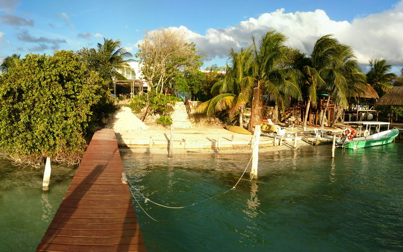 Wooden dock leading to the beachfront Sunset Grill restaurant on Isla Mujeres, palm trees and small boats moored along the calm lagoon shore