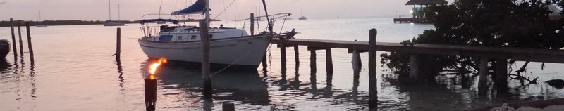 Sailboat moored at a rustic wooden pier at dusk with a tiki torch glowing, waterfront view by the Sunset Grill in Isla Mujeres