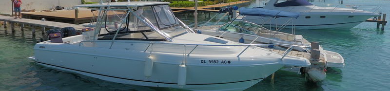 Bote de pesca deportiva Intrepid 32 blanco con hardtop amarrado en el muelle de una marina de Cancún junto a yates más grandes sobre agua turquesa tranquila