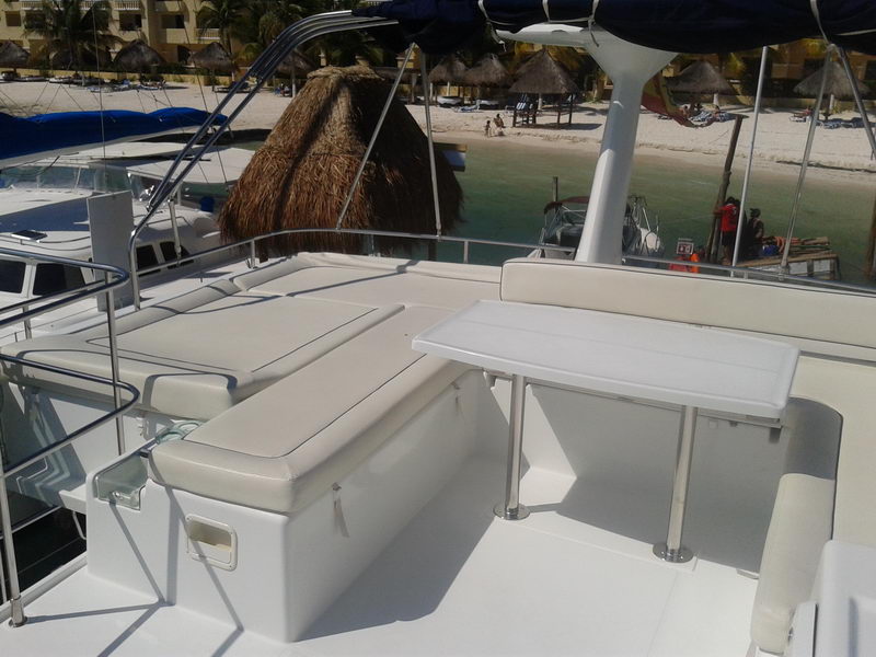 Cushioned flybridge seating and table of the Power Lagoon 46 catamaran moored beside a palapa and white-sand beach near Cancun