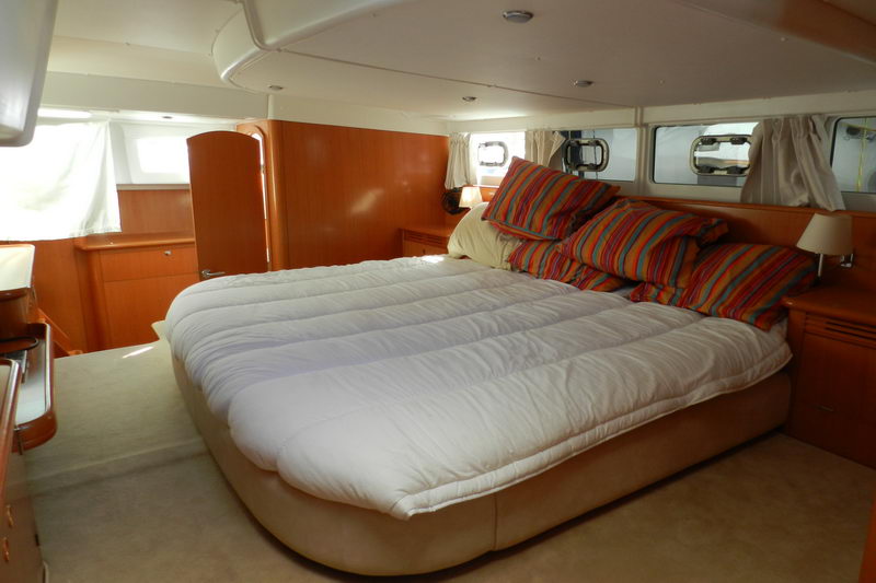 Spacious master stateroom of the Power Lagoon 46 catamaran with king bed, warm wood paneling and striped pillows for overnight Cancun charters