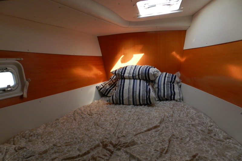 Cozy double guest cabin in the hull of the Power Lagoon 46 catamaran with striped pillows and a porthole, ready for overnight island hopping