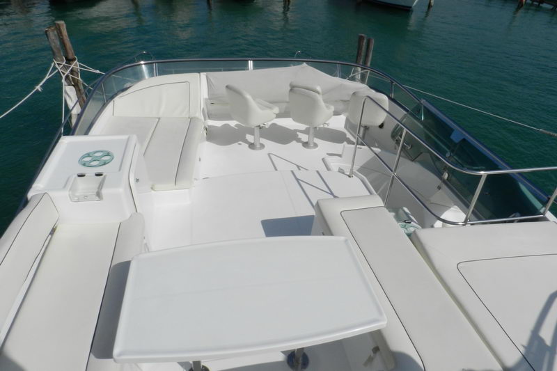 Flybridge of the Power Lagoon 46 catamaran with twin white helm chairs, cushioned sun lounges and a dining table over turquoise Cancun marina water