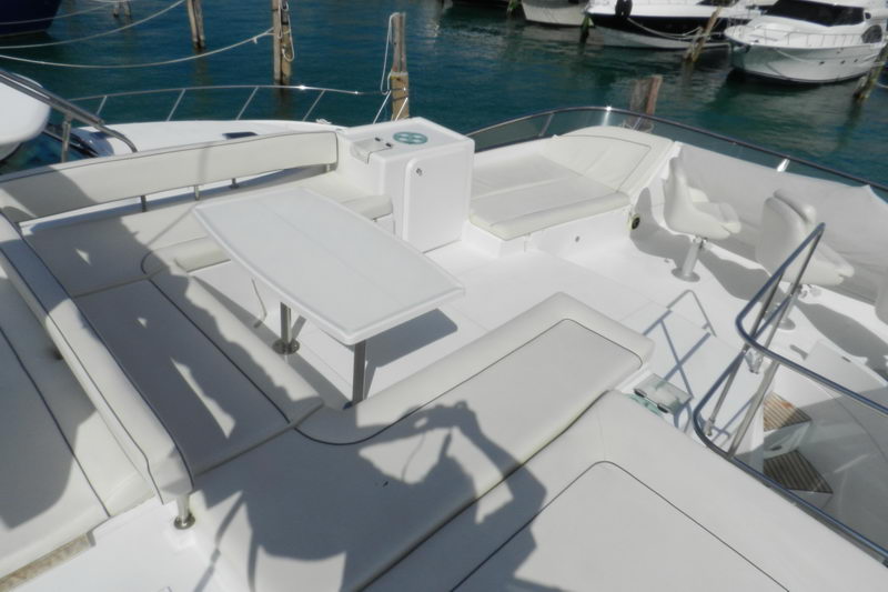 Sunny upper-deck flybridge of the Power Lagoon 46 catamaran with a teak table, wraparound seating and helm chair docked in the Cancun marina