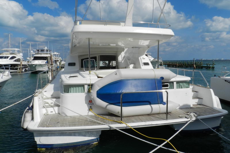 Stern of the navy-trimmed Power Lagoon 46 catamaran with a blue tender on the swim platform, docked over calm turquoise Caribbean water near Cancun