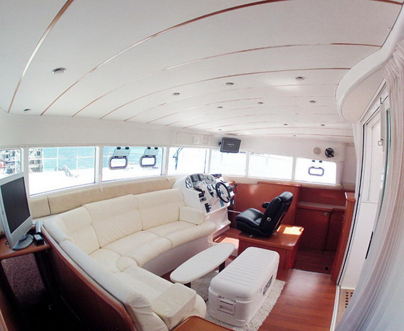 Bright interior saloon of the Power Lagoon 46 catamaran with cream leather sofa, inside helm and wraparound windows over the sea near Cancun