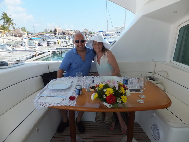 Couple seated at a flower-decorated table in the shaded cockpit of the Power Lagoon 46 catamaran at the Cancun marina, ready for a romantic lunch