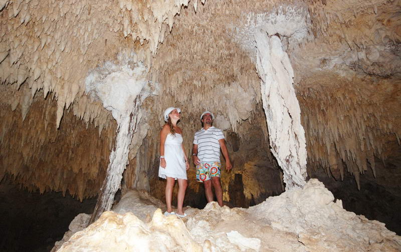 Couple standing on a rock formation inside the vast Aktun Chen dry cave, gazing up at the stalactite-covered ceiling