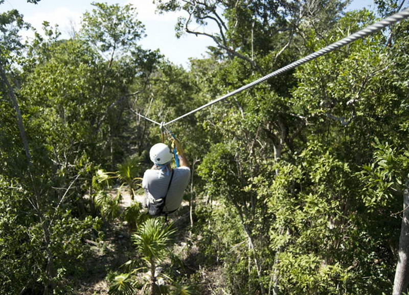 Visitor in a white helmet ziplining away over the dense green jungle canopy at Aktun Chen, Riviera Maya