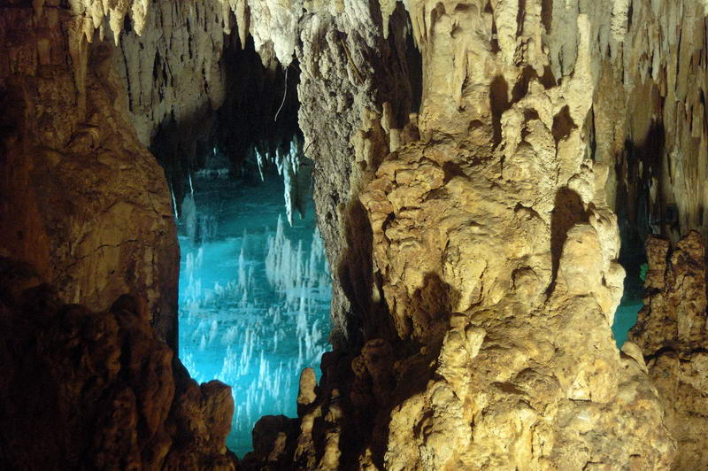 Dramatic stalactite and stalagmite formations framing the glowing blue underground cenote inside Aktun Chen cave