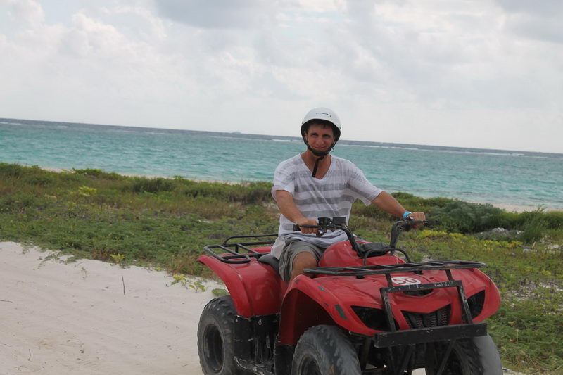 Helmeted rider on a red ATV following a sandy beach trail beside the turquoise Caribbean at Playa Maroma