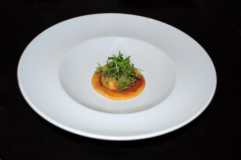 Single ravioli topped with fresh microgreens in a light sauce, plated in a deep white bowl by the Maroma gourmet catering service