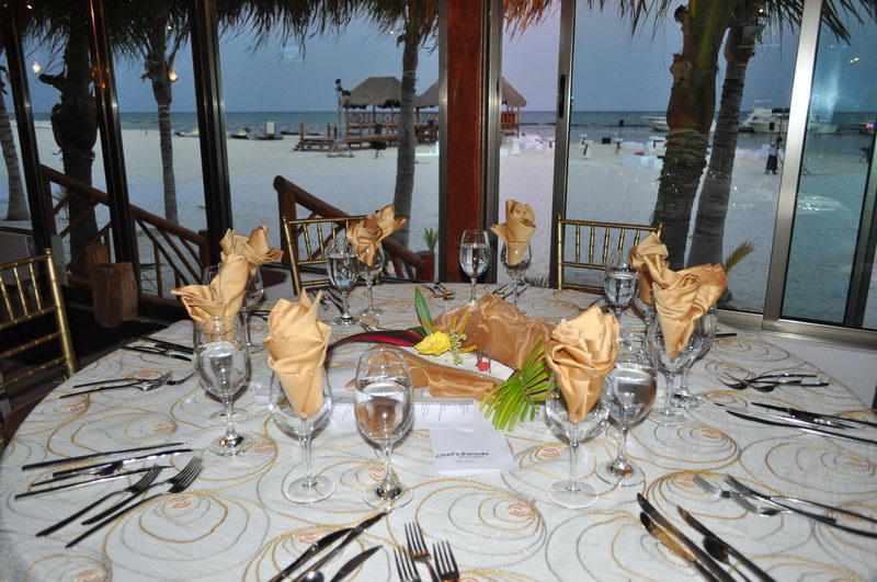 Banquet table dressed with gold napkins facing the white sand beach at dusk, Maroma restaurant event setup, Riviera Maya
