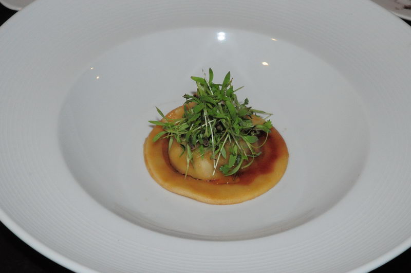 Filled pasta parcel crowned with green sprouts and a glossy sauce in a white rimmed bowl, a Maroma catered gourmet starter
