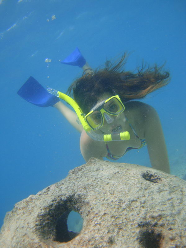 Snorkeler in mask and yellow snorkel glides over a coral head in clear turquoise water on a Maroma reef snorkeling tour, Playa del Carmen