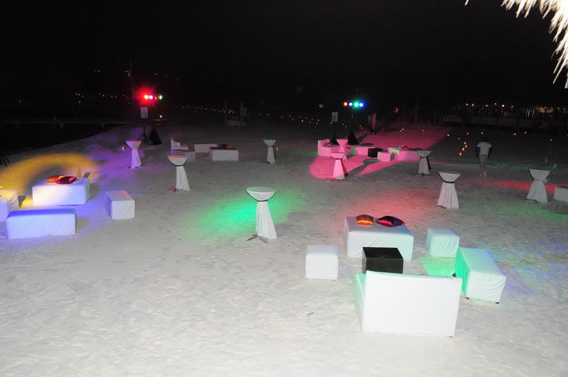 Private beach event at night with white lounge seating, cocktail tables and vibrant party lights on the sand at Marina Maroma, Riviera Maya
