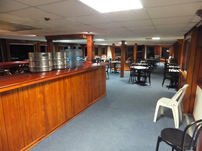 Wood-paneled bar on the Princess boat with beer kegs and water bottles facing a carpeted lounge of café tables