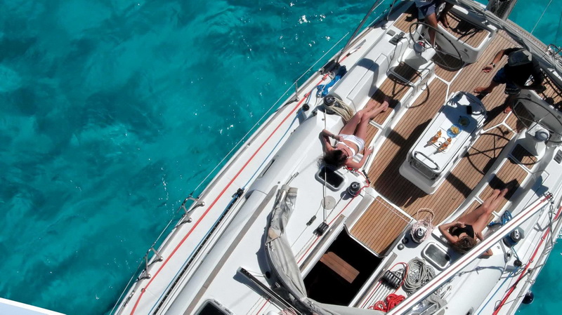 Aerial view of guests sunbathing on teak deck of Jeanneau Sun Odyssey 45 anchored in turquoise Caribbean, luxury charter Cancun